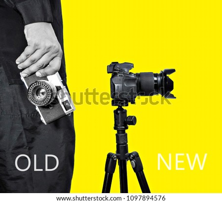 Two different photo cameras, a man hand holding old vintage camera and new camera with tripod on yellow background. Comparison of different generations of photographing equipment. Technology concept.