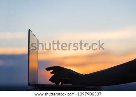 Female hand with laptop on sunset background