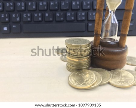 Stack of coins and sandglass on wooden table.