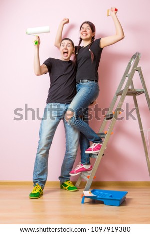 Photo of young woman and man with paint roller standing near staircase