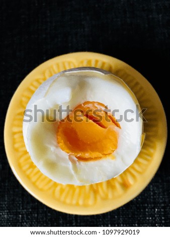 A half white egg in a yellow and orange colored eggcup, with the shape and structure of a half orange fruit in front of black background. The yolk is visible. Picture from top to bottom.