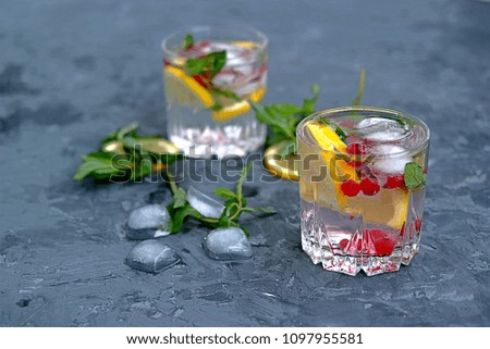 A cool drink, sparkling  water with lemon, red currant, mint and ice in glasses on a dark gray concrete background