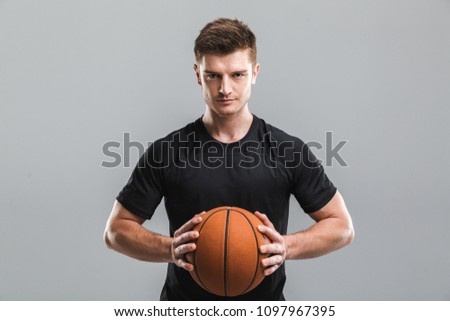 Portrait of a motivated young sportsman holding basketball isolated over gray background