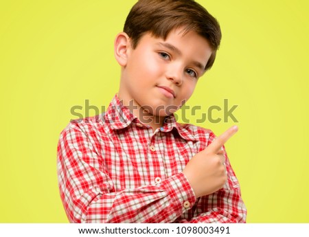 Handsome toddler child with green eyes pointing away side with finger over yellow background