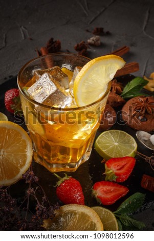 Ice tea in a glass on a black plate with biscuits, sweets and fruits on a black background.