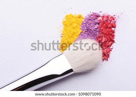 colorful crumbled eye shadow powder and cosmetic brush on a white background