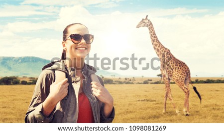 travel, tourism and people concept - happy young woman in sunglasses with backpack over african savannah and giraffe background