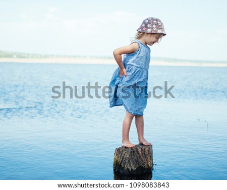 The girl is standing on a stump in the lake