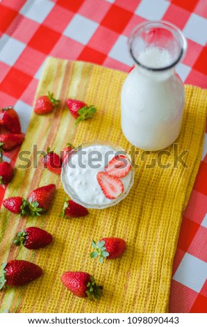 Tasty breakfast, fresh milk in glass bottle, tasty yogurt in small glass bowl with a lot of strawberries around, on yellow kitchen towel, vertical photography, top view