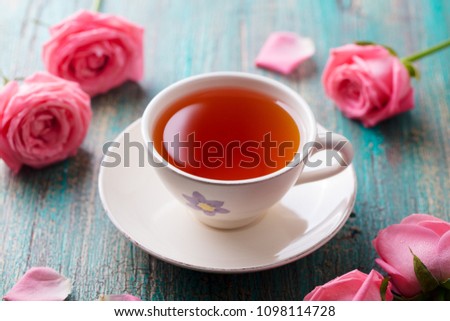 Cup of tea with pink rose. Colorful turquoise wooden background. Close up.