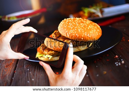 Taking photo on smartphone of traditional American hamburger with a tasty big steak. Burger on a black plate.