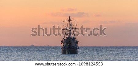 Old wooden sailboat at sunset in the Caribbean sea. Beautiful sky color at twilight. Blue water. Front view.