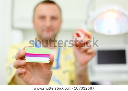 Dentist with artificial jaw shows business card in dental clinic. Shallow depth of field. Focus on card.