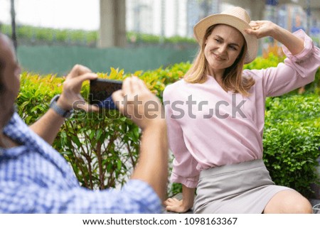 Happy elegant young woman wearing hat posing for photo in park