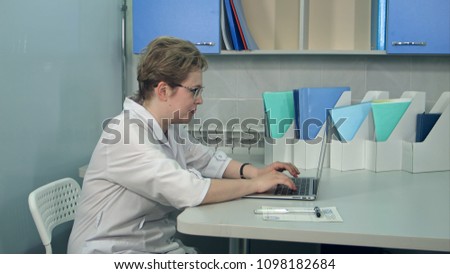 Female doctor in glasses using her laptop computer at clinic