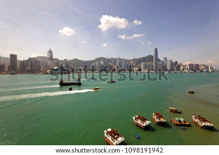 Boats & ships navigate in Victoria Harbor of Hong Kong on a sunny summer day, with the landmark International Finance Center (IFC) Tower standing among skyscrapers before Victoria Peak in background