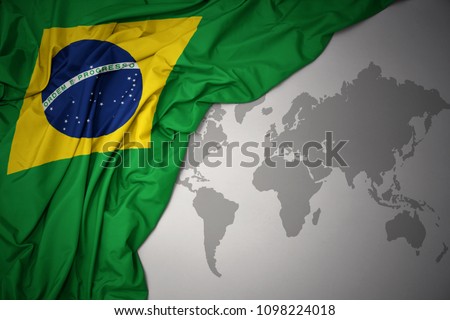 waving colorful national flag of brazil on a gray world map background.