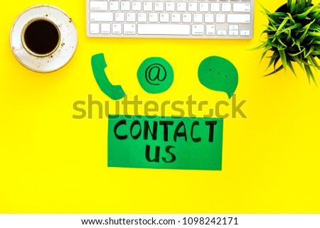 Contact us concept. Lettering Contact us near phone and email signs on office work desk with computer on yellow background top view
