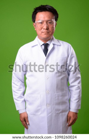 Mature Japanese man doctor wearing protective glasses against green background