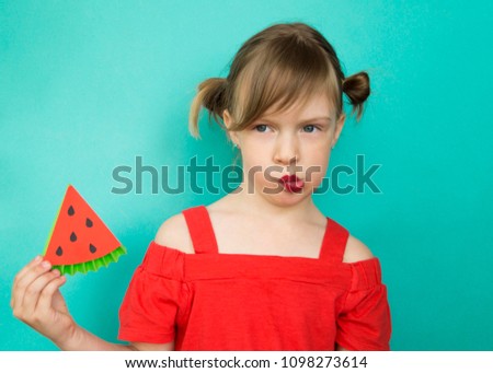 The girl is cheerful in a red dress and with tails on a blue background. Emotions of the child. Hot Summer.A Watermelon.