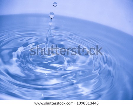 Close up blue water drop falling into water making a reflection concentric circles. Blue wave.