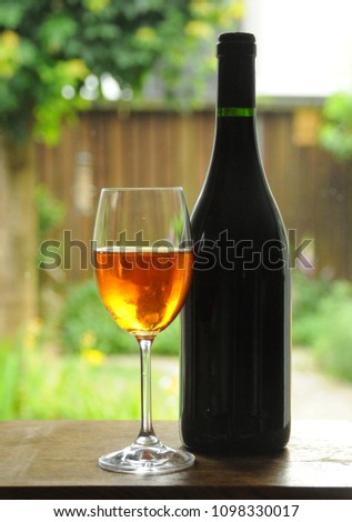 Wine glass with wine bottle and red rose against beige background
