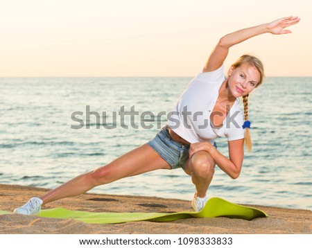 Pretty adult woman in white T-shirt is practicing stretching on the beach