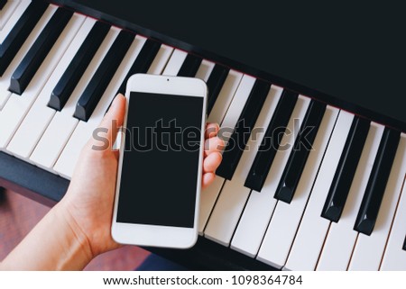 Hand holding smartphone. Mobile with black screen can add text or picture. Piano blurred background.