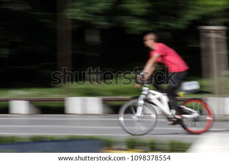 Motion blur picture of man rides bike. Motion blurred photo with rider. Motion picture of man ride a bike in a park background. Blurred wallpaper with people do sports