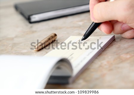 Male Hand Filling out  Cheque on the Table Royalty-Free Stock Photo #109839986