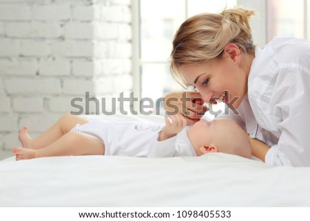 Family portrait of mom and baby in white clothes on the bed.