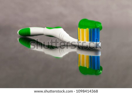 A toothbrush with a toothpaste with herbs of green color applied on it with a reflection on a gray abstract background with a great depth of field.