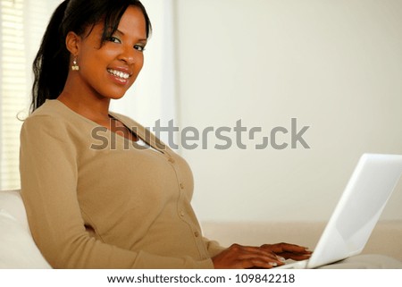 Portrait of a pretty girl smiling at you while working on laptop at home indoor