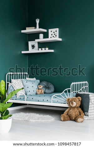 Teddy bear toy by a white twin bed in a dark green room interior for a child with white decor and a plant