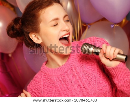 Lifestyle concept: Happy singing girl. Beauty redhair woman with microphone over  background of balloons. 