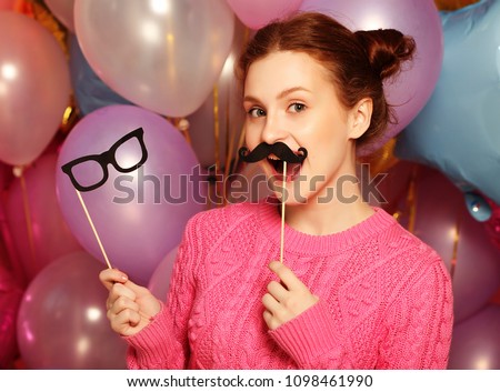 Party concept: happy girl with  fake mustaches and glasses. Background of with many colorful balloons.