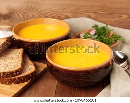Two brown bowl of pumpkin soup on brown dark wooden background, side view.