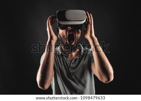 A bearded man screams and touches the head, using a helmet of virtual reality. Black background