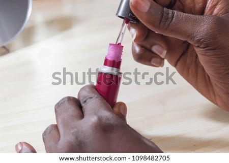 Black woman's Hand holding open liquid lipstick on dresser table with mirror