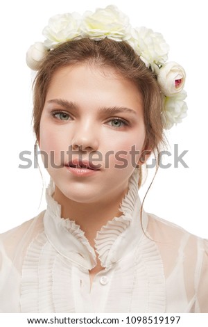 Portrait of a young lady with a bridal flower crown, in a retro blouse. The pretty girl looking pensively at the camera on the white background, tilting her head, white peonies and roses in her hair.