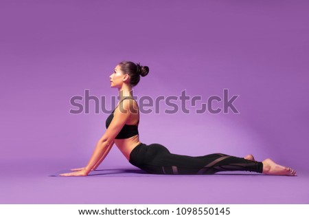 Long haired beautiful pilates or yoga athlete does a graceful pose while wearing a tight sports outfit against a bright purple background in a studio Royalty-Free Stock Photo #1098550145