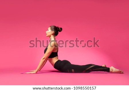 Long haired beautiful pilates or yoga athlete does a graceful pose while wearing a tight sports outfit against a pink background in a studio Royalty-Free Stock Photo #1098550157