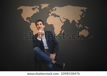 Dreaming big concept. Young man making plans and visualizing the future results in his imagination having an abstract world map on a gray wall on background. Dreams to travel all over the world.