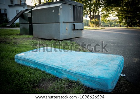 Used mattress thrown out and left by a dumpster for trash.