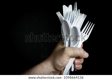 Disposable plastic silverware in a bundle; in hand on dark backdrop.