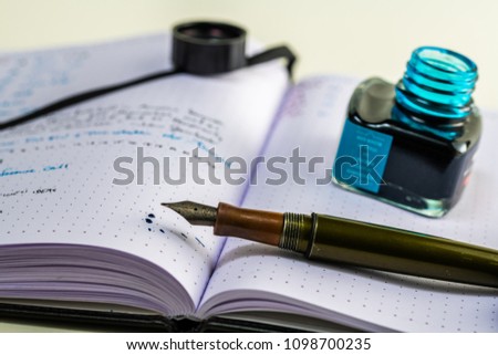 Notebook with writing and a fountain pen with blue ink, ink splattered on the paper making a mess and a large blue ink blot