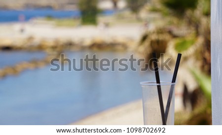 empty plastic cup with straws in the foreground with blurred seascape
