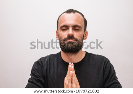 a man with a beard and a black t-shirt meditates with his hands folded