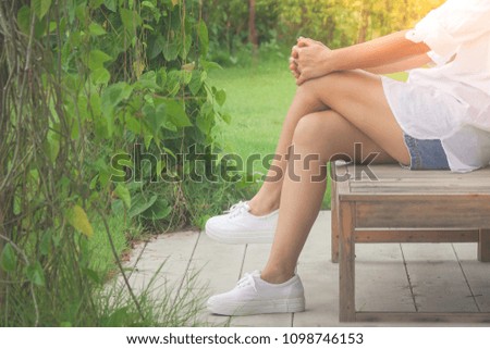 Woman wear white shirt and blue jean shorts. She sitting relax on wooden long chair in the garden. (Selective focus)