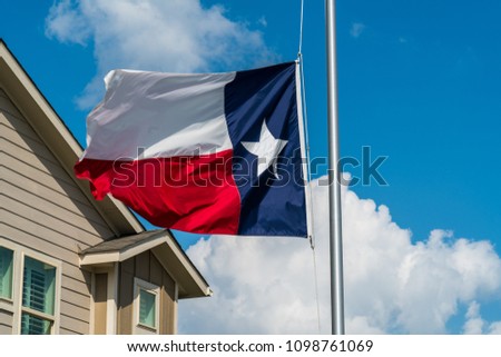 Texas state flag flying lowered at Half Mast right before Memorial Day Weekend with perfect blue sky sunny day with modern new house rooftop in corner of image
